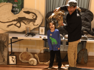 Dinosaurs Rock Birthday Party Instructor Placing Cave Bear Skull over Birthday Child head