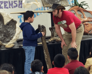 Dinosaurs Rock instructor demonstrating with Birthday Child the size of Dinosaur Bones at a Dinosaurs Rock Birthday Party