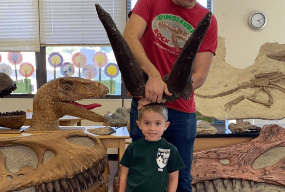 dinosaurs rock instructor placing triceratops horns on birthday boys head with various dinosaur fossils in background