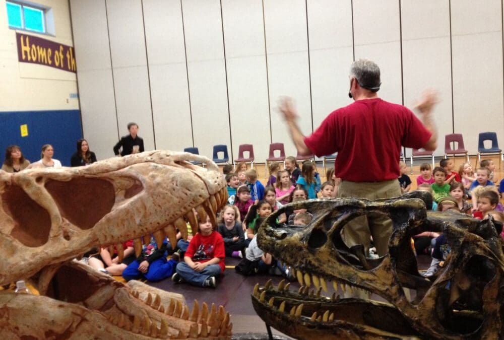 dinosaurs rock instructor speaking to students with a Tarbosaur Dinosaur Skull and a Allosaurus Dinosaur Skull featured in front